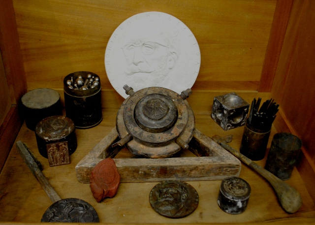 De izda. a dcha. y de detrs a delante: tiles para batir el metal. Modelo de la medalla de Menndez Pidal.  Molde para el batido de metal. Punzn. Anverso Escuela Po.  til para el cincelado de punzones y troqueles. Martillo de cincelador.  Cinceles. Re